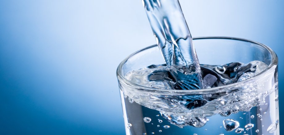 Pouring water into glass on blue background