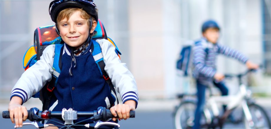 Two school kid boys in safety helmet riding with bike in the city with backpacks. Happy children in colorful clothes biking on bicycles on way to school. Safe way for kids outdoors to school