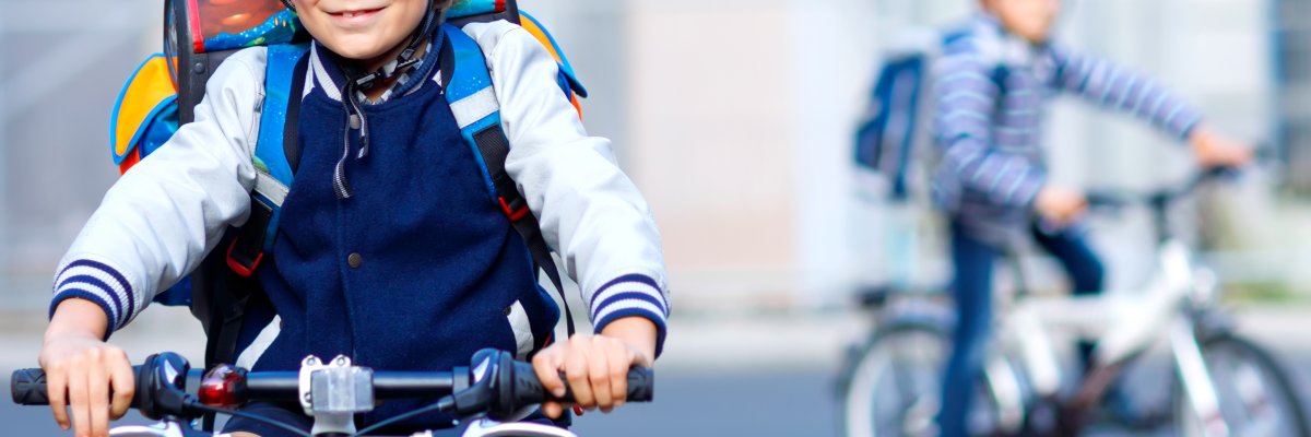 Two school kid boys in safety helmet riding with bike in the city with backpacks. Happy children in colorful clothes biking on bicycles on way to school. Safe way for kids outdoors to school Two school kid boys in safety helmet riding with bike in the city with backpacks. Happy children in colorful clothes biking on bicycles on way to school. Safe way for kids outdoors to school