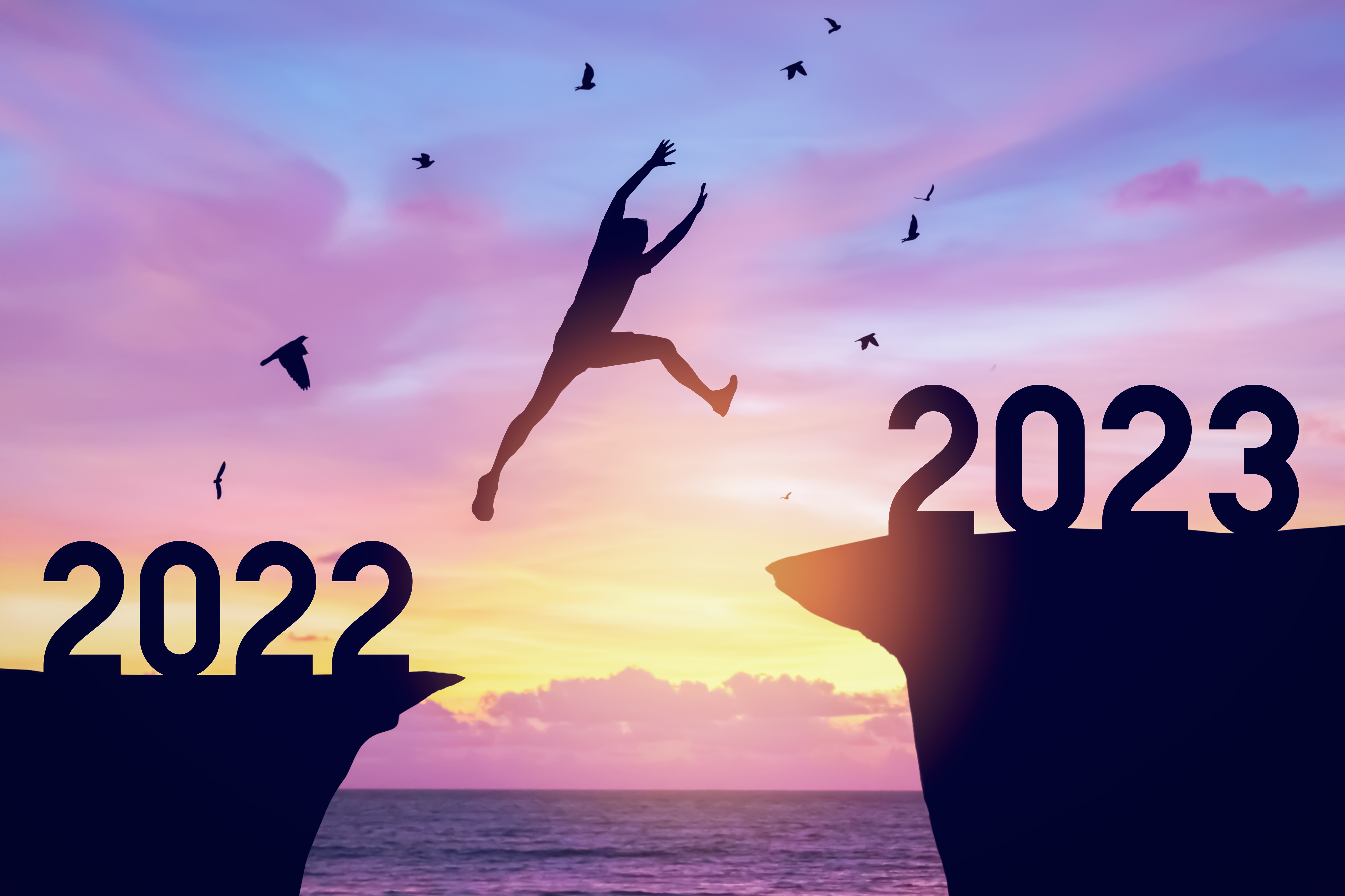 Silhouette man jumping between cliff with number 2022 to 2023 an