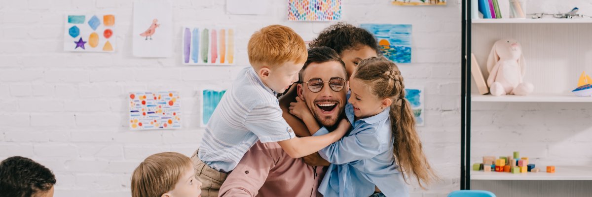 interracial kids hugging happy teacher at table in classroom interracial kids hugging happy teacher at table in classroom
