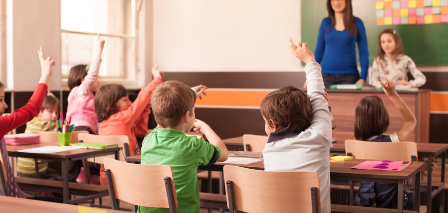 Children in elementary school are raised hand in clasroom